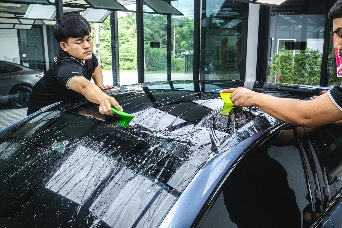 ช่างสองคนใช้ที่รีดไล่น้ำใต้ฟิล์มกันรอย SCP Skyshield บนหลังคารถเก๋งสีดำ